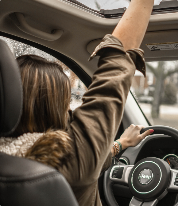 A woman sits in the driver seat of a car with her arm raised in the air in excitement