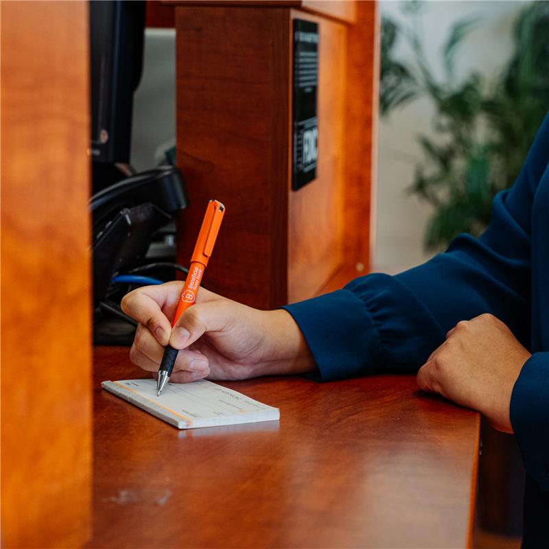 Hand writing check at teller station with orange pen