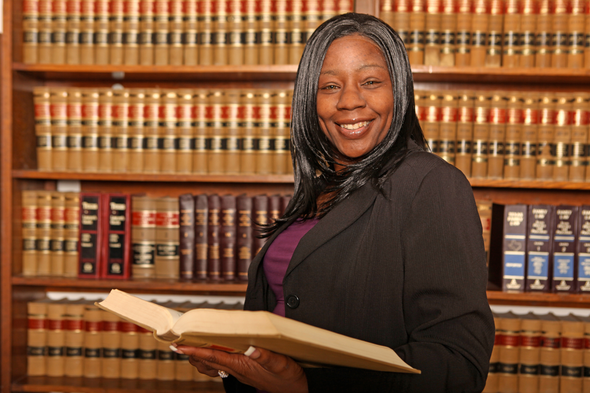 Professionally dressed woman stands with legal book in front of a wall of bookshelves