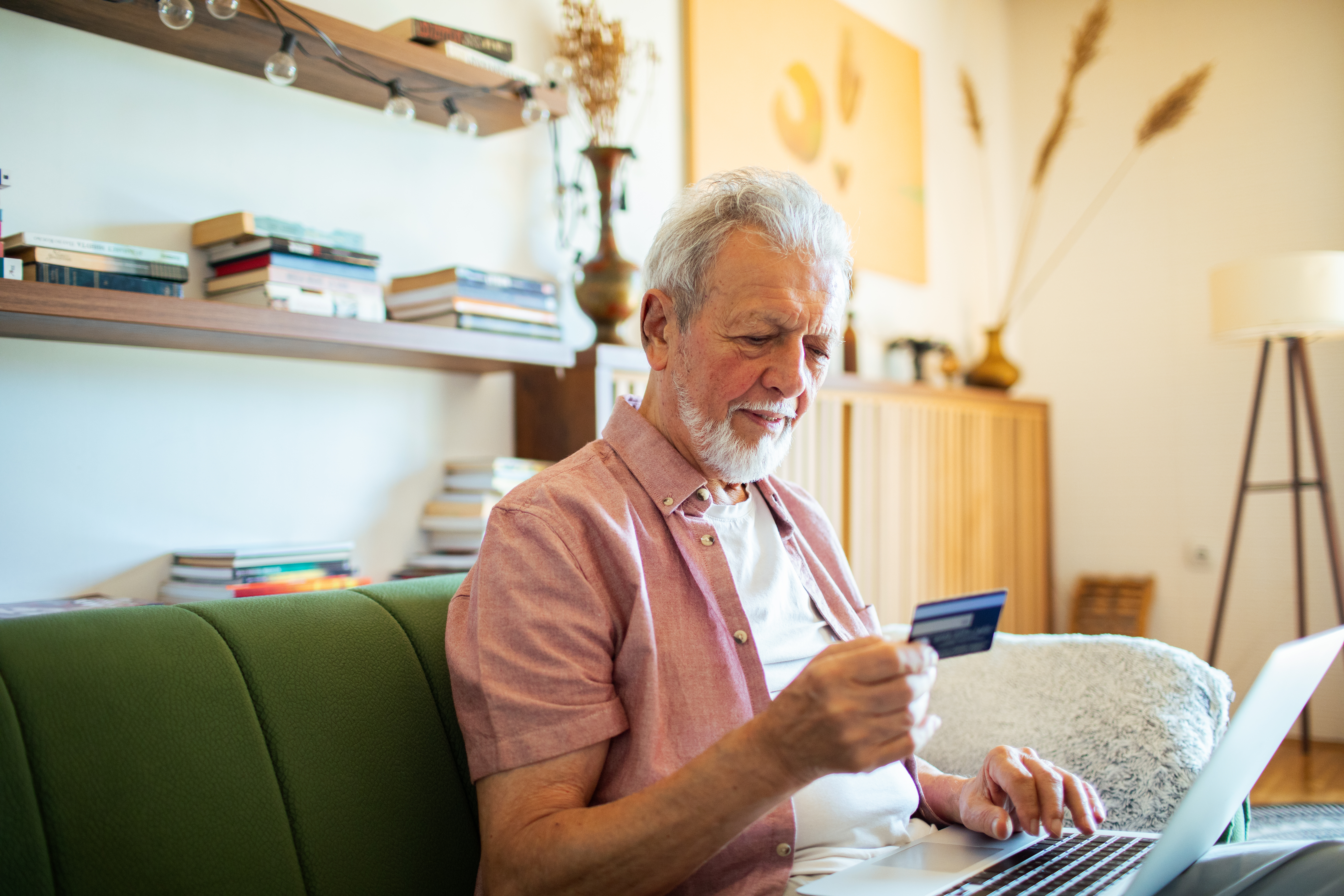 Man Sitting on Couch with Laptop Looking at Credit Card