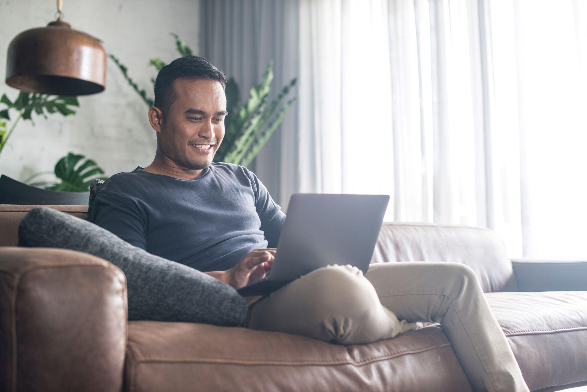 Man sits on couch using his computer and looking up his routing number