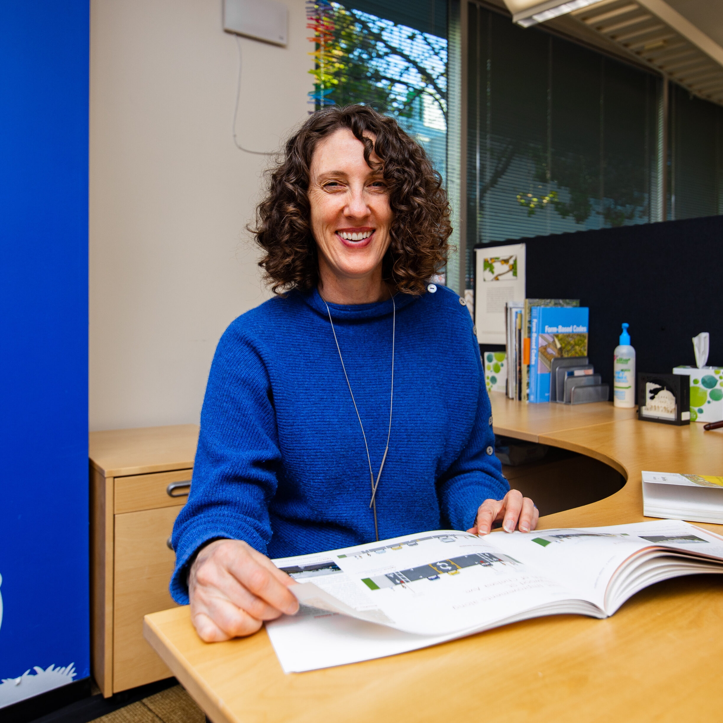 Karen Parolek sits at her desk in a blue sweater in front of a blue wall with a white bicycle painted on it.