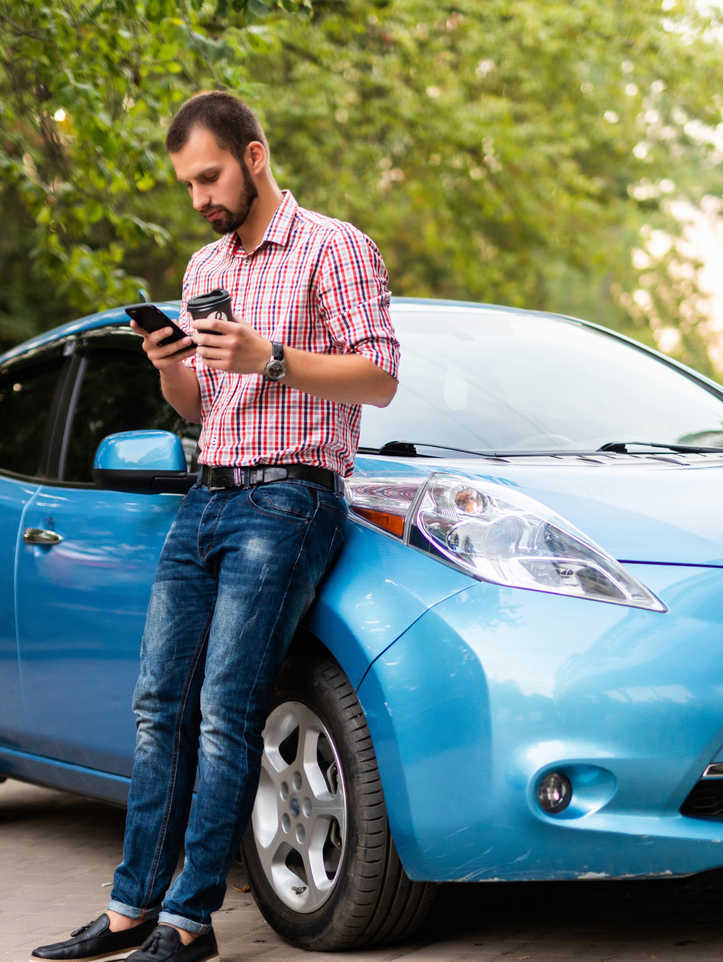 A man looks at his phone while standing next to a blue electric vehicle charging