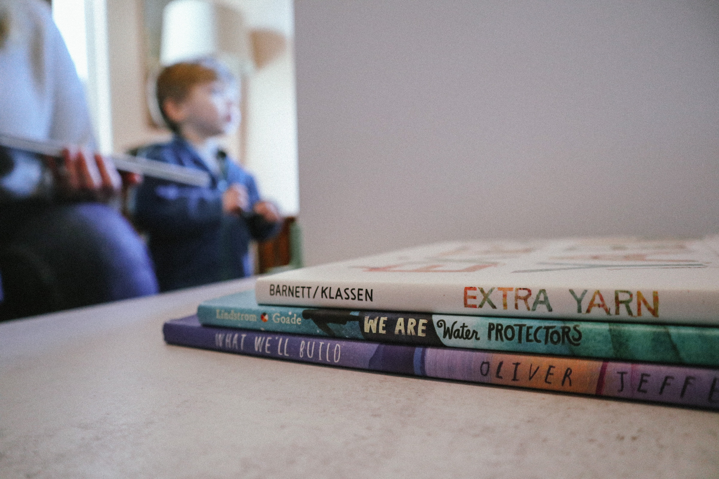 A child is out of focus in the background. In the foreground we see three children's books on a table.