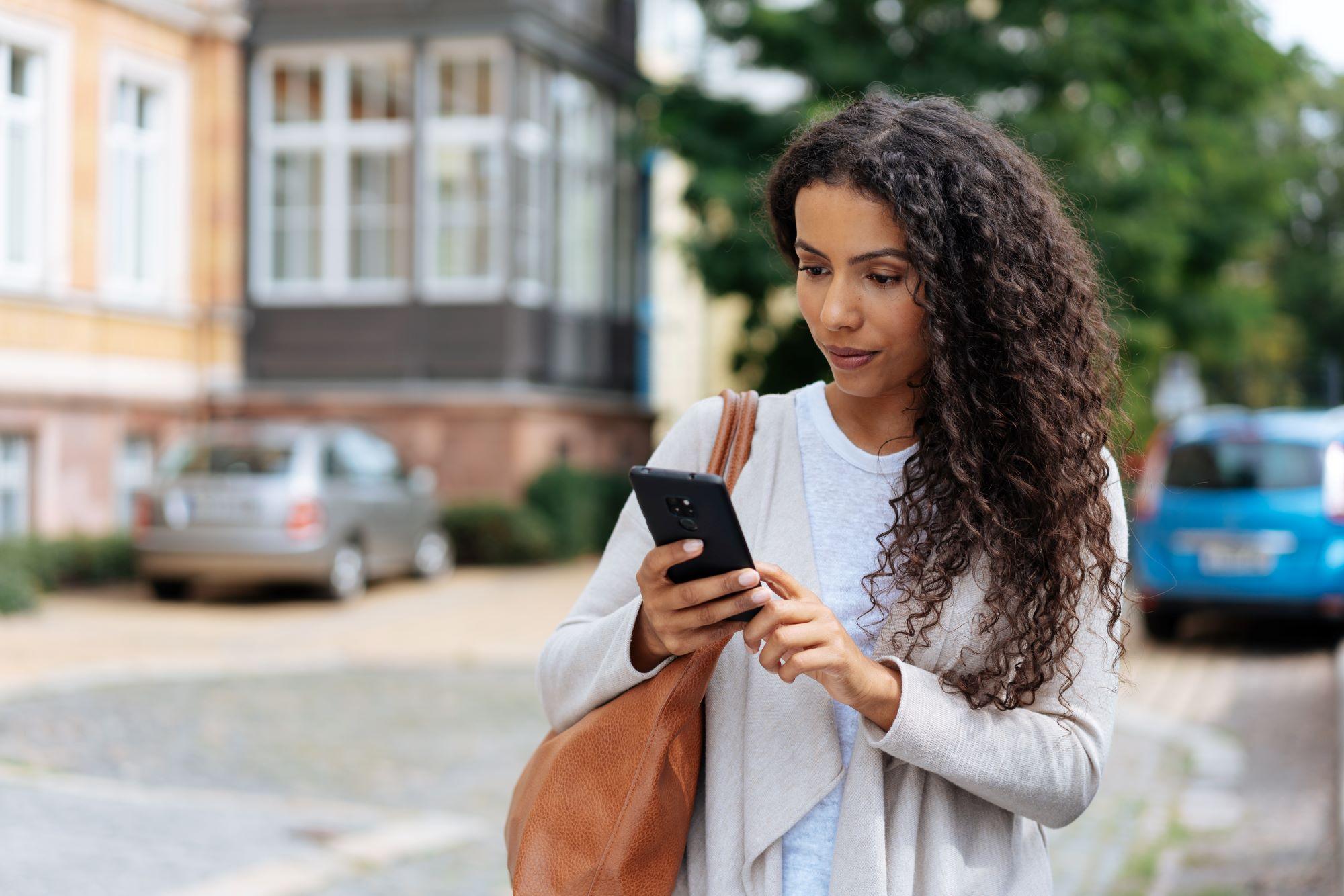 Woman stands on the street and looks at her phone to find her account number