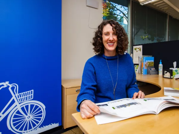 Karen Parolek sits at her desk in a blue sweater in front of a blue wall with a white bicycle painted on it.