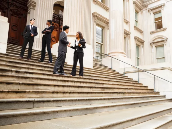 4 people in suits stand on courthouse steps talking