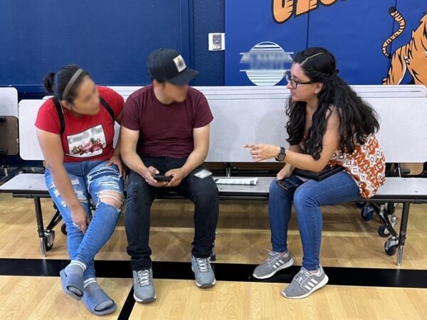 One of Entidad's staff members Sofia Gago speaks with two people whose faces are blurred, as part of Entidad's community outreach efforts.