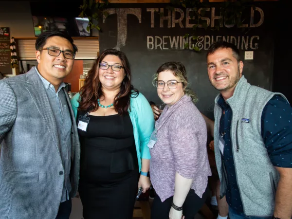 Four People Smiling, with a Threshold Brewing Blending sign in the background