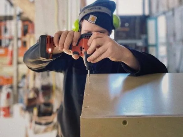 Person wearing ear protection and a warm hat using a drill to add screws to a project