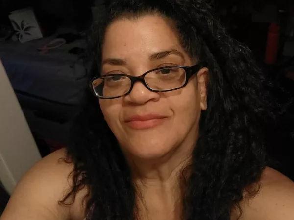 Photo of Alicia smiling, in glasses, with hair half up and half down.