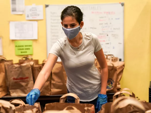 Food Bank volunteer packs bags for pick-up, wearing a mask. Photo credit Alabastro Photography