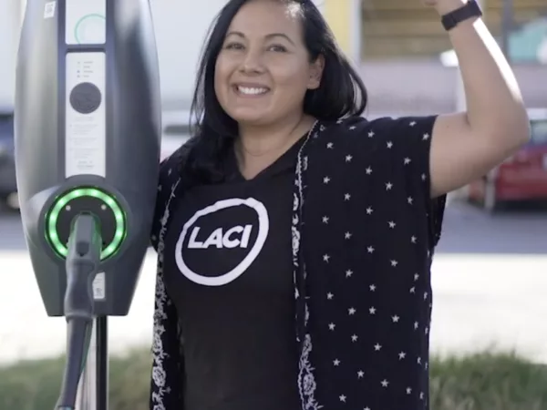 A person standing next to an electric car charger in a LACI t-shirt in a power pose.