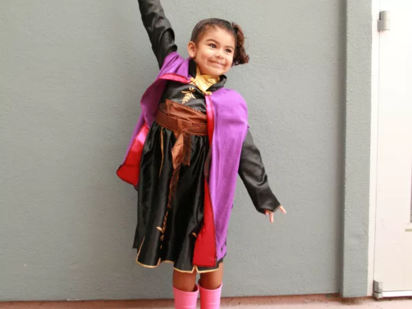 A smiling young girl in pink boots stretches her arms (one up and one down).