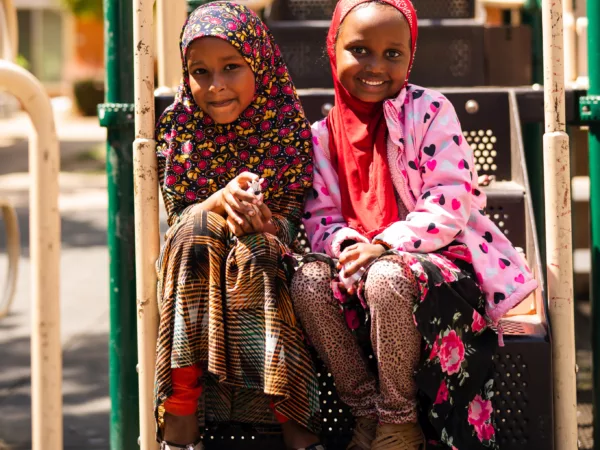 Two girls in hijab sit on a playground smiling at the camera. Photo by Christine Dong.