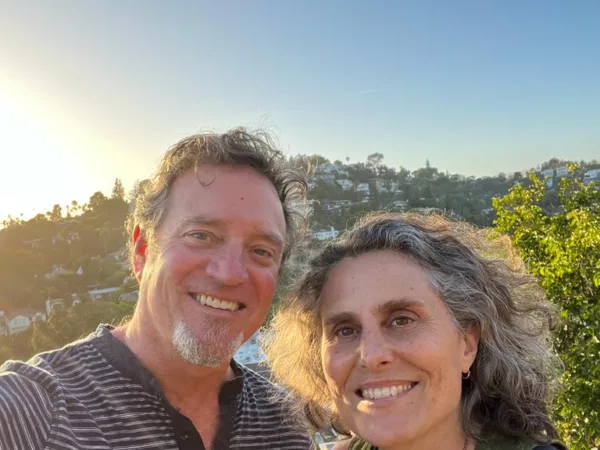 A selfie of Mark (left) and Mara (right) co-founders and publishers of Neighbor2Neighbor, both smiling at the camera with the Los Angeles hills in the background