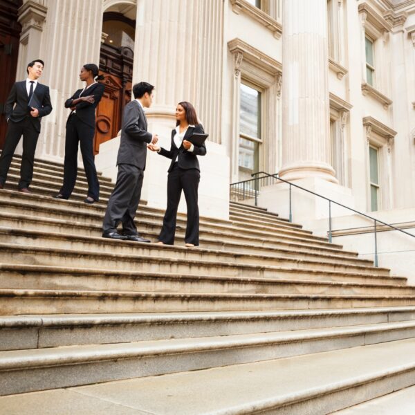 4 people in suits stand on courthouse steps talking