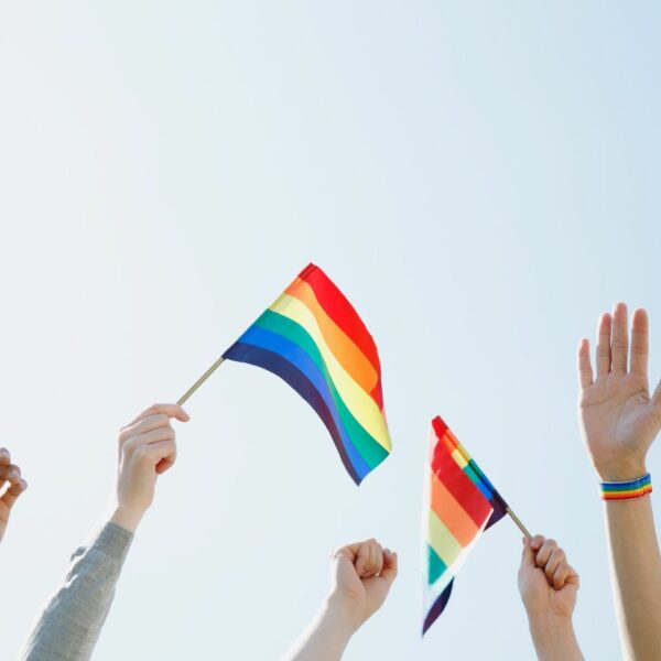 Hands holding small Pride flags against a clear blue sky