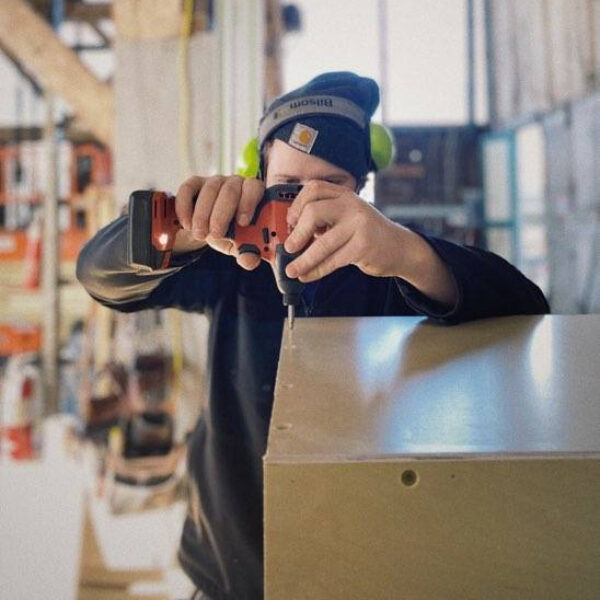 Person wearing ear protection and a warm hat using a drill to add screws to a project