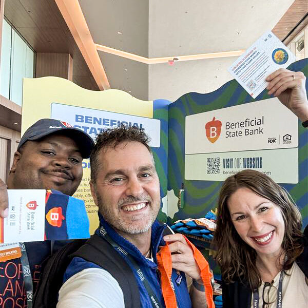 Beneficial State Bank employees holding merch in front of a booth at Champions Retreat