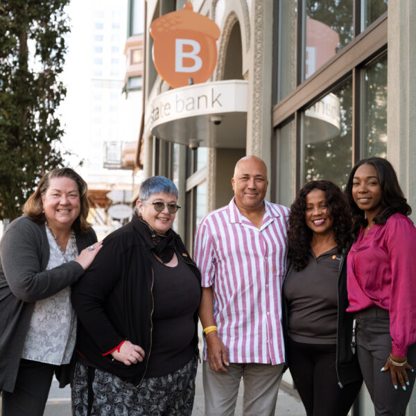 A group of Beneficial State Bank staff standing in front of the Oakland branch sign, smiling at the camera.