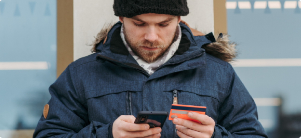 Man wearing winter clothes holds his phone and a credit card