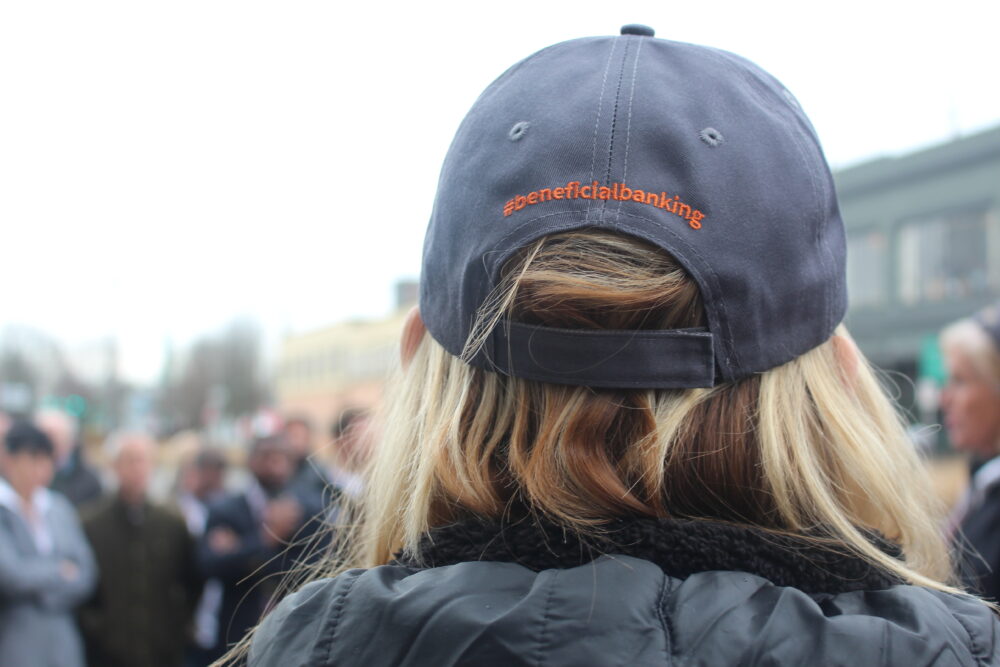 A woman wears a navy blue baseball cap that says #beneficialbanking in orange stitching on the back