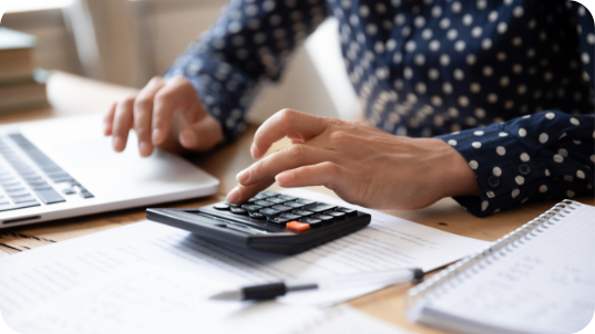 Close Up Of Woman's Hands Using A Calculator And Her Computer