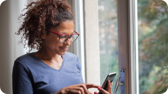 Woman Wearing Glasses Looking At Her Phone And Smiling